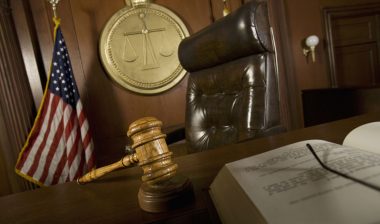 A gavel and an open book sit on a judge's bench.