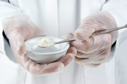 A lab tech holds a spoonful of white powder.