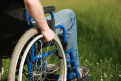 A man sits in a wheelchair by a field.