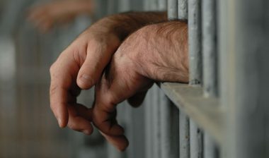 Close-up of man's hands behind bars