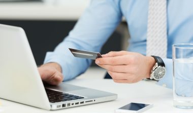 A man types at a laptop while holding a credit card.