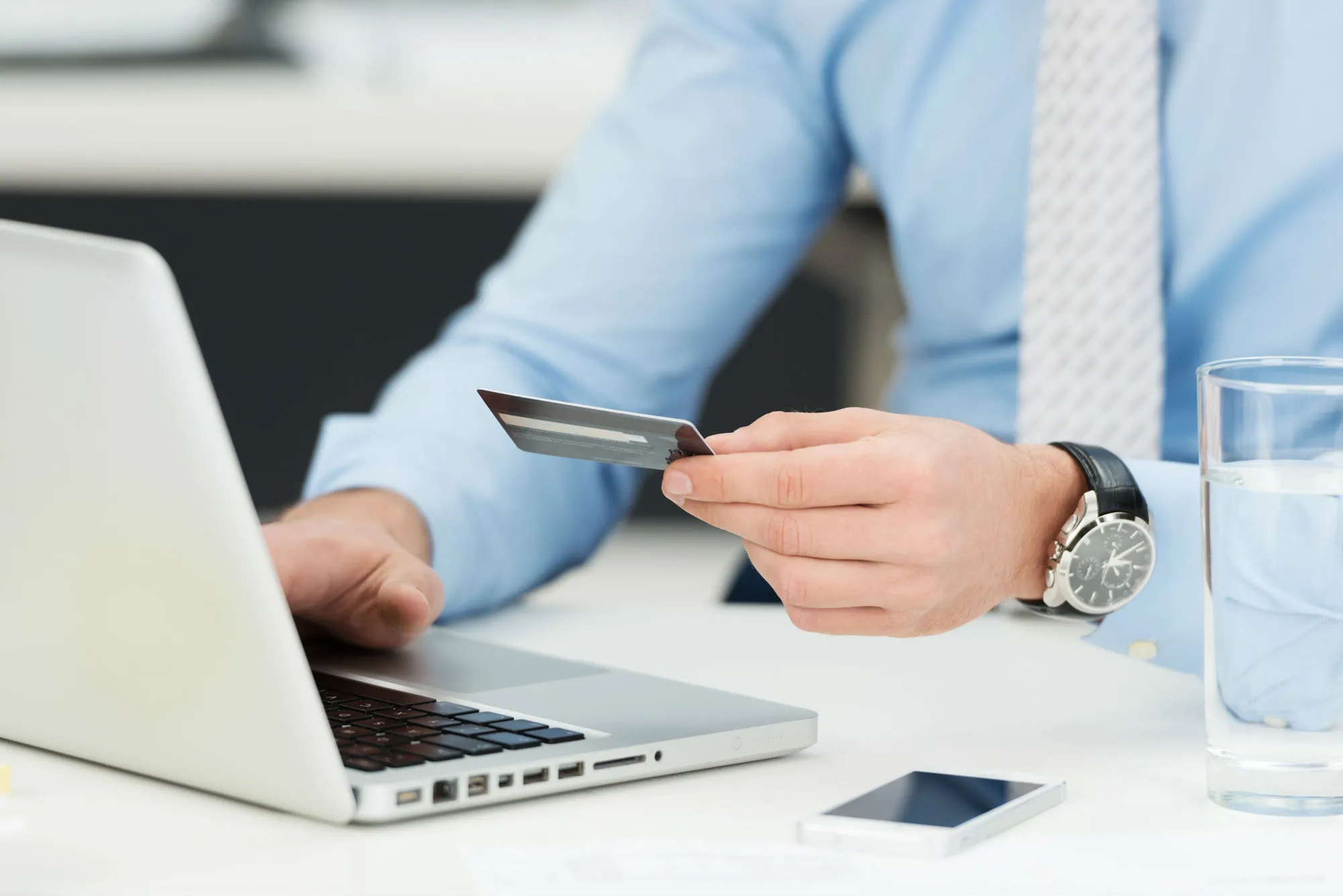A man types at a laptop while holding a credit card.