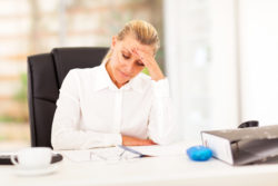A woman at a desk holds her head in her hand.