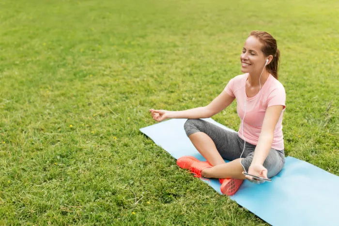woman listening to simple habit podcast on her smartphone while meditating in the park