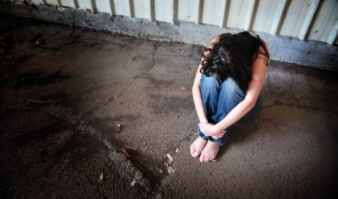 A woman sits alone with her head on her knees.