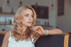 A woman sits and holds her glasses.