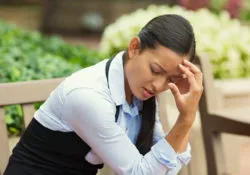A woman sits on a bench and holds her head.