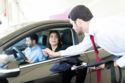 A salesman talks to a couple in a car.