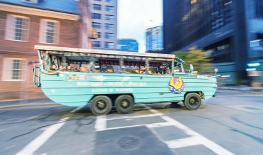 A duck boat drives through a city.
