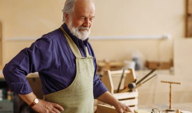 Elderly man wearing carpenter smock with hip pain