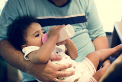 A baby girl is fed from a bottle.