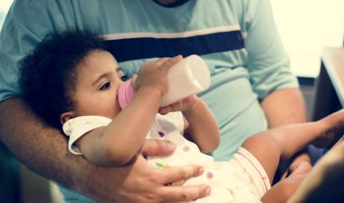 A baby girl is fed from a bottle.