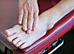 A patient on an exam table touches their foot with their hand.