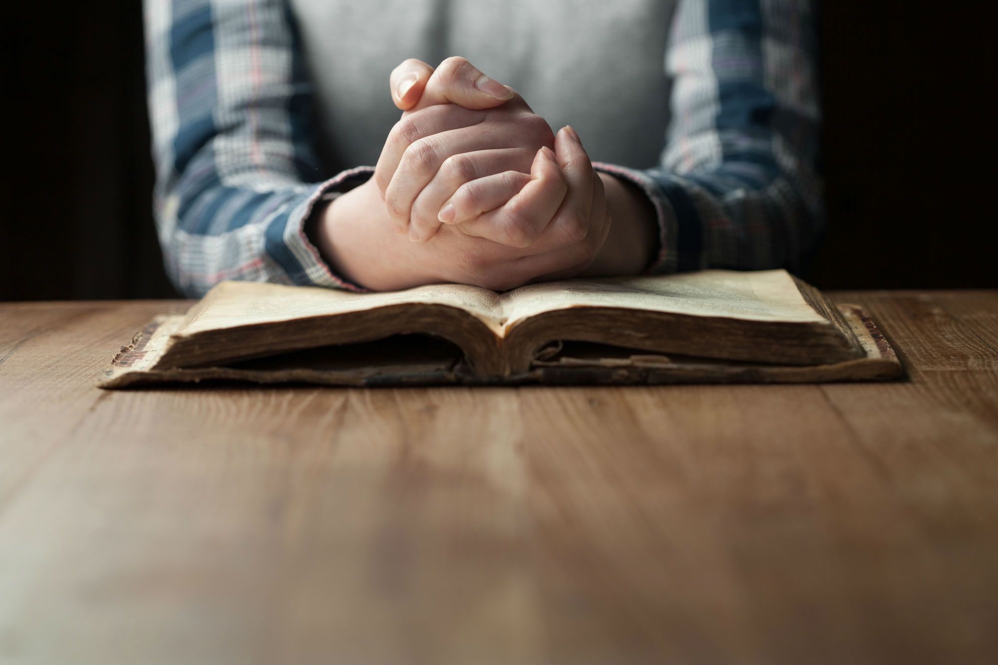 A woman prays with her hands on a bible.
