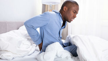 A young man in bed shows signs of back pain.
