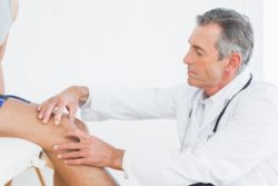 older doctor examines knee pain of patient