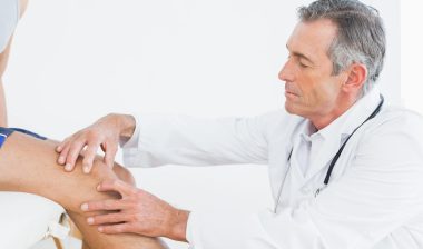older doctor examines knee pain of patient