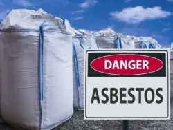 An asbestos warning sign next to bags of asbestos