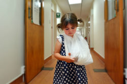 A little girl with a broken arm walks down a hall.