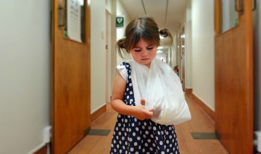 A little girl with a broken arm walks down a hall.