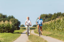 A couple rides bicycles on a dirt path.