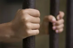 Two hands hold prison bars.
