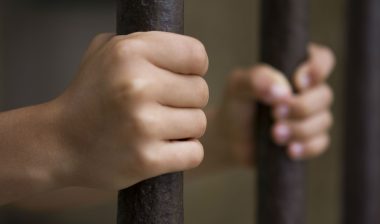 Two hands hold prison bars.