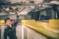 A mechanic examines the undercarriage of a truck.