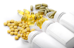 Supplement capsules spill out of three white bottles.