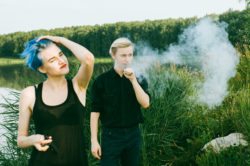 Two teens vape by a lake.