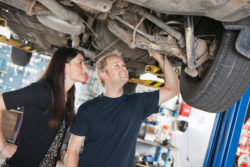 A couple inspects the undercarriage of a vehicle.