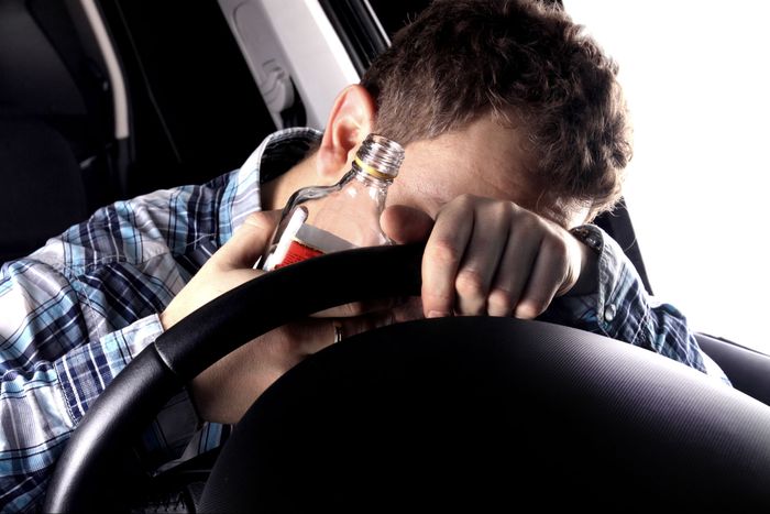 drunk man with open bottle of liquor slumps over steering wheel