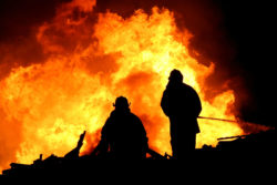 Two firefighters work on a fire at night.