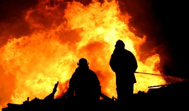 Two firefighters work on a fire at night.