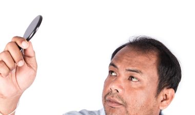 Man looking at thinning hair with small mirror