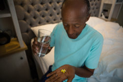A man takes pills while sitting on a bed.