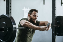 A man uses a smartphone while leaning on freeweights.
