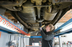 A mechanic works beneath a truck on a lift.
