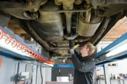 A mechanic works beneath a truck on a lift.