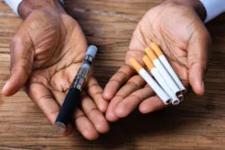 Hands hold e-cigarettes and traditional cigarettes.