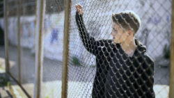 Boy reflects on being detained at CoreCivi Laredo stares through chain link fence.