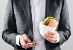 A man holds a smartphone and a sandwich.