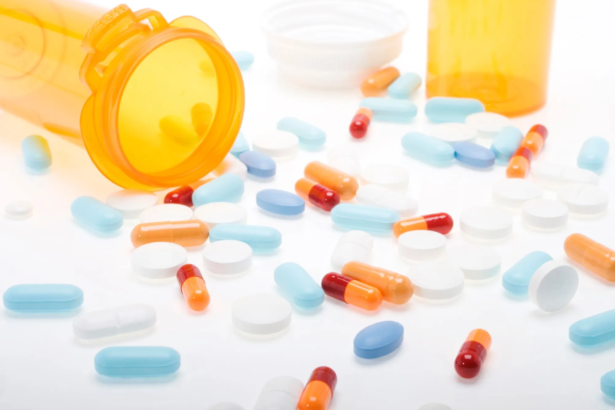 Orange bottle and multicolored pills on white counter