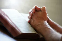 Folded hands rest on an open bible.