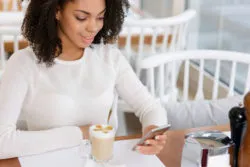 A woman sitting at a table looks at her smartphone.