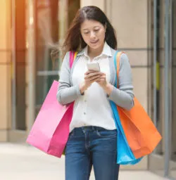 A woman texts while holding shopping bags.