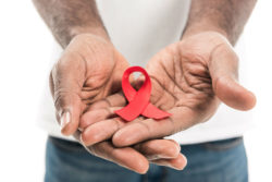 Two hands hold a red ribbon for HIV awareness.