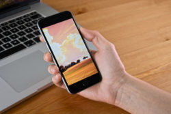 iPhone in a hand with a laptop behind it