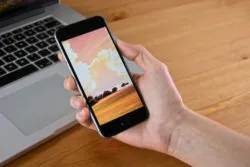 iPhone in a hand with a laptop behind it