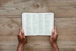 man holding holy bible over wooden table